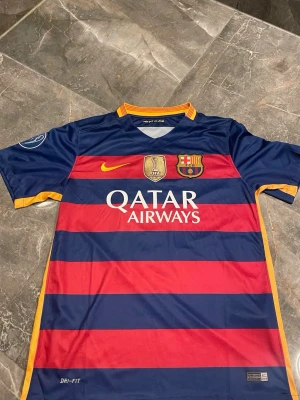 FC Barcelona matchtröja Nike - Säljer en officiell FC Barcelona matchtröja från Nike med breda blå och röda ränder, gula detaljer och Qatar Airways som sponsortryck. Tröjan har klubbmärke, FIFA-märke och Dri-FIT-material för bra ventilation. Perfekt för dig som älskar fotboll och Barca!