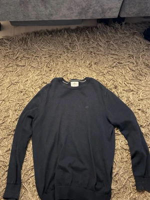 Mörkblå tröja från Morris - Snygg mörkblå tröja från stansfield med rund halsringning och diskret logga på bröstet. Tröjan har långa ärmar och ribbade muddar vid ärmslut och nederkant. Perfekt för en stilren och enkel look. Nypris:899