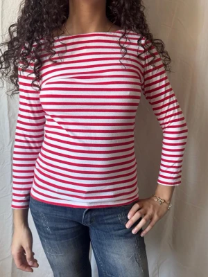 Randig långärmad topp röd och vit - Snygg långärmad topp med röda och vita horisontella ränder. Klassisk båtringad hals och figurnära passform. Perfekt för en fräsch och stilren outfit nu till våren. Storlek xs men är strechig så passar även S.