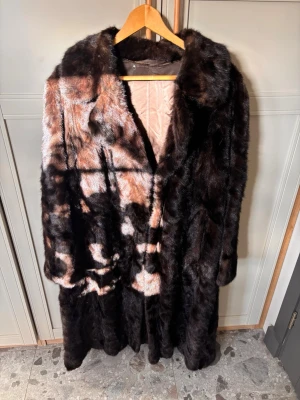 Lång mörkbrun minkkappa - Snygg lång kappa i mörkbrun med mjukt foder och bred krage. Pälsen har ett glansigt, lyxigt utseende och ger en riktigt trendig vintagekänsla. Perfekt för dig som vill sticka ut och hålla dig varm under kalla dagar. 