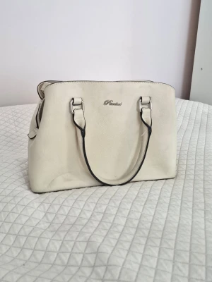 Beige handväska Puccini/Rizzo - Säljer denna eleganta handväska från Puccini/Rizzo!💘 Oklart om det är äkta läder eller inte. Finns extra axelband och många olika fack inuti! Lite smuts på undersidan, annars mycket gott skick🫶 Passa på, fri frakt en vecka fom. 15/2 
