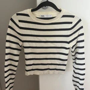 Randig croppad tröja från Zara - Snygg croppad tröja från Zara i vitt med svarta ränder. Tröjan har rund halsringning och långa ärmar. Perfekt för dig som gillar en klassisk men trendig look. Materialet är mjukt och stretchigt för en bekväm passform. Sitter croppad och kan vara lite magtröja