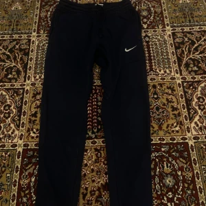 Svarta Nike mjukisbyxor med logga - Säljer ett par svarta mjukisbyxor från Nike med klassisk vit logga på vänster ben. Byxorna har dragsko i midjan och raka ben. Perfekta för chill dagar eller träning. Tillverkade i mjukt material för extra komfort.