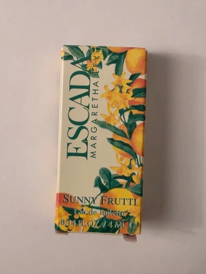 Escada Sunny Frutti Eau de Toilette - Fräsch parfym från Escada, Sunny Frutti, i en elegant ljusgrön flaska med guldfärgat lock. Förpackningen har färgglada citrus- och blomdetaljer som ger en somrig känsla. Flaskan rymmer 4 ml och har en lyxig, vintageinspirerad design.