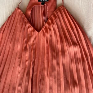 Plisserat, korallfärgat linne Express - Superfint plisserat festlinne från Express i en snygg korallton. Linnet har tunna axelband och v-ringning. Perfekt för dig som gillar en luftig och trendig look.