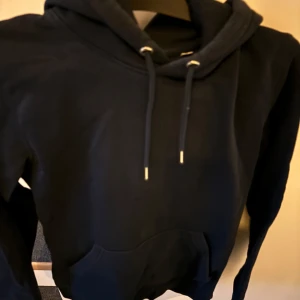 Marinblå  hoodie med tryck Mi Amor - Marinblå hoodie med huva och dragsnören. På ryggen finns ett vitt tryck med texten 'Mi Amor' och ett hjärta genomborrat av en pil. Hoodien har en klassisk känguruficka framtill och är i mjukt material, perfekt för en chill och avslappnad stil.