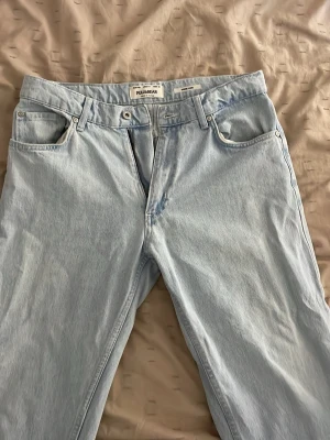 Ljusblå raka jeans från Pull&Bear - Säljer ett par ljusblå jeans från Pull&Bear med rak passform och klassisk femficksdesign. Jeansen är tillverkade i denim och har bälteshällor samt knappgylf. Perfekta för en avslappnad och trendig look.