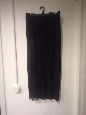 Svart långkjol i chiffong - En svart långkjol med rak passform och lätt transparent material som ger ett flowy intryck. Kjolen har enkel design utan synliga detaljer och passar perfekt till olika stilar. Materialet känns tunt och luftigt.