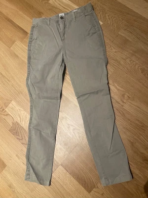 Khaki chinos från GAP stl XS - Snygga khaki chinos från GAP med klassisk rak passform och bälteshällor. Byxorna har två sidofickor fram och två passpoalfickor bak. Tillverkade i mjukt bomullstyg som ger en skön känsla och stilren look.