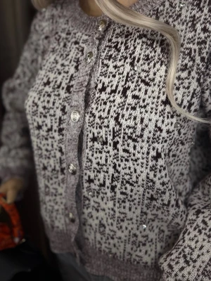 Mönstrad stickad kofta med knappar S-M - Säljer en mysig stickad kofta i grått och svart med unikt mönster. Koftan har rund halsringning, långa ärmar och silverfärgade knappar framtill. Ribbstickade muddar vid ärmslut och nederkant ger en skön passform. Perfekt för lager på lager och snygg till jeans.