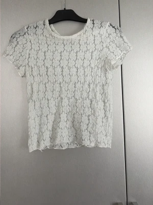 Vit spetsblus med blommönster - Säljer en vit blus i spets med korta ärmar och rund hals. Blusen har ett detaljerat blommönster över hela tyget och är lätt transparent. Perfekt för dig som gillar romantiska och feminina toppar. Storlek 164 men är jätte stretchig som gör att den passar upp till m! 