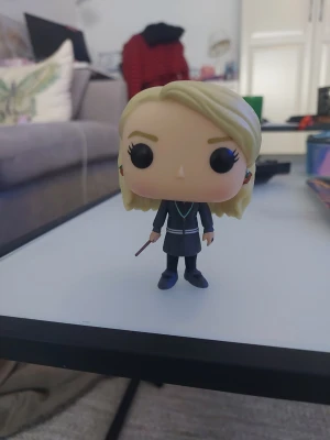 Funko Pop figur med trollstav  - Cool maskerad- och cosplayfigur från Funko Pop med blont hår, svart uniform och trollstav. Perfekt som accessoar till Harry Potter-tema eller cosplay. Figuren har stora svarta ögon och klassisk Funko Pop-stil.