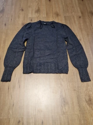 Mörkgrå stickad tröja från Only - Mysig mörkgrå stickad tröja från Only med puffärmar och breda ribbade muddar vid ärmslut och nederkant. Tröjan har rund halsringning och en klassisk rak passform, perfekt för lager på lager under kyliga dagar. I bra skick och är knappt använd.