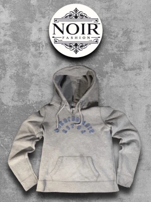 Grå hoodie Abercrombie & Fitch - Snygg grå hoodie från Abercrombie & Fitch med blå broderad text på bröstet. Klassisk känguruficka framtill och justerbar huva med dragsko. Perfekt för en avslappnad och trendig look.