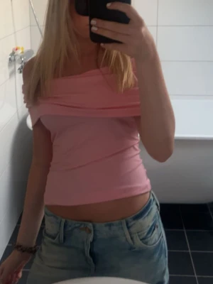 Ljusrosa offshoulder topp - Trendig ljusrosa offshoulder topp med croppad passform. Toppen är ärmlös och har en bred kant över axlarna som ger en snygg och modern look. Perfekt att matcha med jeans för en avslappnad stil.