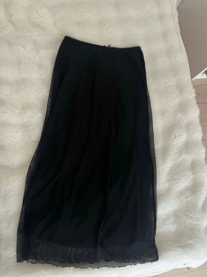 Svart långkjol Lågmidjad från H&M Divided - Svart långkjol Lågmidjad från H&M Divided med lätt transparent ytterlager och rak passform. Kjolen har en enkel och stilren design som passar perfekt till många olika looks. Materialet känns mjukt och följsamt mot huden.