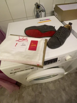 Gråa Christian Louboutin sneakers - Snygga gråa sneakers från Christian Louboutin med den ikoniska röda sulan. Skorna har lågt skaft, klassisk snörning och är tillverkade i mocka. Perfekta för dig som vill ha något exklusivt och stilrent i garderoben. PRIS GÅR ATT DISKUTERA 