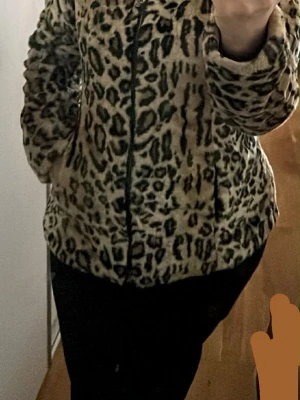 Leopardmönstrad pälsjacka Giovanna - Säljer en fluffig pälsjacka från Giovanna med leopardmönster i beige, svart och brunt. Jackan har dragkedja framtill, hög krage och två sidofickor. Perfekt för dig som vill sticka ut och hålla dig varm under vintern.