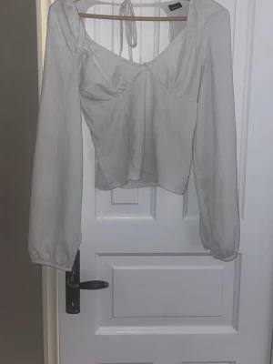 Vit långärmad blus med knyt - Snygg beige blus med långa ärmar och knyt i nacken. Toppen har en lätt croppad passform och en feminin v-ringning. Säljer då den inte kommer till användning, passar mig som vanligtvis har XS-S