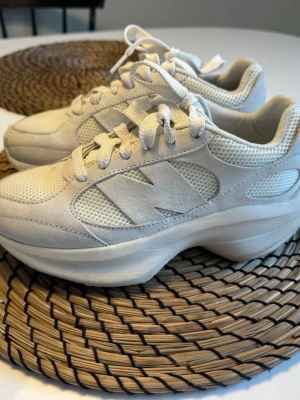 Vita New Balance sneakers i mocka och mesh - Stilrena vita sneakers från New Balance. Använda ca 4 gånger. Finns en fläck på toppen se bild. Går säkert bort med galltvål. Annars i fint skick. 