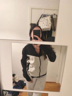 Nike zip hoodie svart och grå - Säljer en snygg zip hoodie från Nike i svart och ljusgrått. Tröjan har dragkedja framtill, huva med snören och Nike-logga på bröstet. Perfekt för en sportig och avslappnad stil. Materialet är mjukt och bekvämt, troligen bomullsblandning.