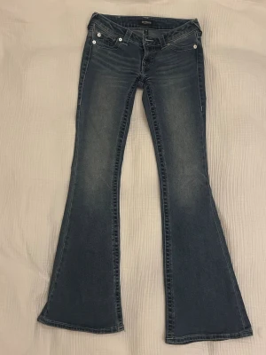 low waist bootcut jeans från True Religion - Säljer ett par blå low waist bootcut jeans från True Religion med klassiska kontrastsömmar och fem fickor i modellen Joey. Nästan aldrig använda då dom inte passar mig. Innebenslängd 79 och midjemått 37