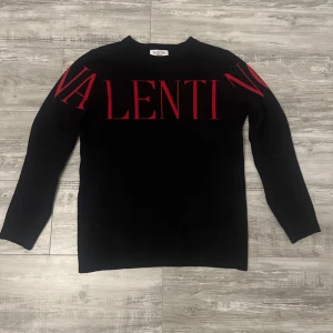 Valentino tröja  - Svart stickad tröja från Valentino med röd logotyp över bröstet och axlarna. Tröjan har rund halsringning och långa ärmar. Snygg och stilren design som sticker ut med den stora röda texten. Perfekt för dig som gillar exklusiva märken och vill ha något unikt.