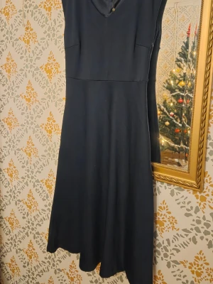Mörkblå ny festklänning från Kaffe - En stilren mörkblå klänning från Kaffe med v-ringning och ärmlös design. Klänningen har en lätt utställd kjol och slät yta som ger ett elegant intryck. Perfekt för dig som gillar enkel men snygg stil. Liknar klänning från ralph laurent.  nypris 899kr Storlek S, tts
