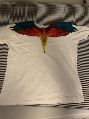 Marcelo burlon (äkta) storleken är m men passar s  - Unik vit t-shirt från Marcelo Burlon County of Milan med färgglada vingar i blått, rött och gult tryck över axlar och bröst. Klassisk passform och rund halsringning. Perfekt statement-plagg för dig som vill sticka ut.