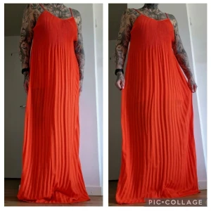 Plisserad orange maxiklänning - Snygg långklänning i stark orange färg med tunna axelband och plisserad design. Klänningen har en lös passform och är perfekt för varma dagar. Materialet känns lätt och luftigt, vilket ger en skön känsla.