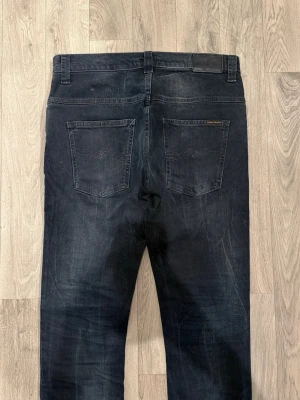 Nudie Jeans Slim/Straight Mörkblå/Svart W32/L32 - Slim Fit - Mycket fint skick. Storlek W32/L32 (Modellapp avklippt). Mått - Midja: 42,5cm, Ytterbenslängd: 109cm, Benöppning: 17,5cm. Modellen är 185cm & 63kg. Hör av dig vid funderingar!🤝