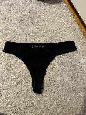 Calvin Klein stringtrosa – svart - Snygg och minimalistisk stringtrosa från Calvin Klein med ikonisk logga i midjan. Mjuk och stretchig kvalitet som sitter bekvämt hela dagen och ger en osynlig passform under kläder.
