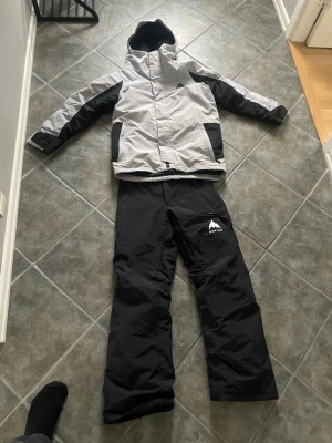 Skidställ från Burton  - Säljer ett par svarta täckbyxor från Burton i storlek XL. Byxorna har en klassisk passform med logga på vänster lår och är tillverkade i slitstarkt, vattenavvisande material. Perfekta för skidåkning eller snowboard och håller dig varm under kalla dagar. Barn XL- ca storlek 170