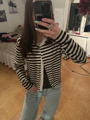 Randig svartvit kofta med knappar - Snygg svartvit randig kofta med rund hals och knäppning framtill. Koftan har långa ärmar och smala ränder, samt ribbade muddar vid ärmslut och nederkant. 