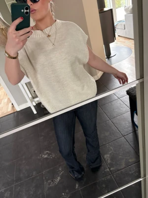 Beige stickad väst med kort ärm - Snygg beige stickad väst med korta ärmar och rund halsringning. Västen har en avslappnad passform och ribbstickade kanter vid ärmslut och nederkant. Perfekt att styla över en skjorta eller t-shirt för en trendig lager-på-lager-look. Från only. 