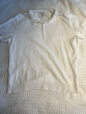 Vit pikétröja från H&M - Säljer en klassisk vit pikétröja från H&M med krage och två knappar framtill. Tröjan är kortärmad och har ribbad nederkant. Perfekt för dig som gillar en clean och enkel stil. Materialet är mjuk bomull som känns skönt mot huden.