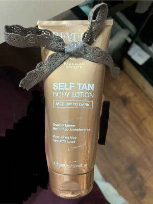 Self Tan Body Lotion  - Brun-utan-sol lotion från Revolution i nyansen Medium to Dark. Ger gradvis solbrun färg, är oparfymerad och kladdfri. Innehåller återfuktande aloe vera och har en fräsch, lätt doft. Tuben rymmer 200 ml och har en snygg bronsfärgad design. Rosett kan tas bort😅tyckte bara de var lite sött✨helt oanvänd!!! Hoppas de går att se! Helt NY! 👀🎉brun utan sol är dyrt, men jag säljer billigare😀för jag vet att jag själv gillar det🤪
