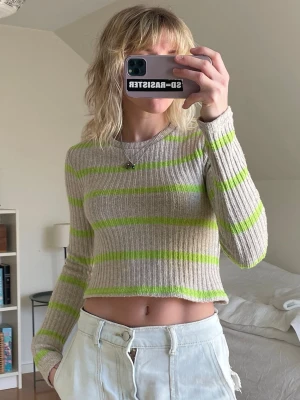 Beige och grön randig croppad topp - Randig croppad topp i beige och ljusgrön med ribbad struktur och långärmad design. Perfekt för dig som gillar en avslappnad och trendig stil. Materialet känns mjukt och stretchigt, vilket gör den bekväm att bära.