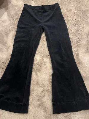 Svarta utsvängda mjukisbyxor - Säljer ett par svarta mjukisbyxor i mjuk velour med utsvängda ben. Byxorna har hög midja och är perfekta för en chill och avslappnad stil. Inga synliga loggor eller detaljer, bara klassiskt snygga och bekväma.