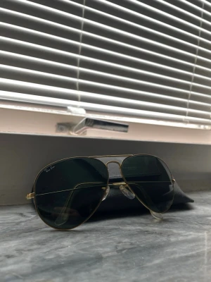 Ray-Ban aviator solglasögon guld - Klassiska Ray-Ban aviator solglasögon med tunna guldfärgade metallbågar och mörkgröna glas. Snygg och tidlös modell som passar till alla outfits. Kommer ej med originellt fodral för att det är borta. 
