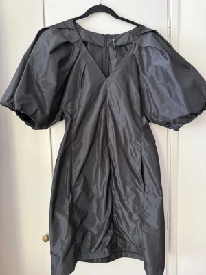 Svart  puffärmad klänning Inwear  - Snygg svart  klänning i från Inwear Ladybird med puffiga korta ärmar och v-ringning. Klänningen har dragkedja i ryggen och är tillverkad i ett glansigt syntetmaterial som ger en cool look. Perfekt för dig som vill sticka ut med en unik siluett.strl 42