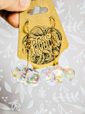 Iridescent pärlörhängen moln bubblor guldpläterade  - Unika örhängen från strössel med kluster av iriserande pärlor i akryl som reflekterar regnbågens färger. Krokarna är i guldpläterad metall och har en modern, lekfull design som verkligen sticker ut. Perfekta för dig som vill ha något annorlunda och trendigt.