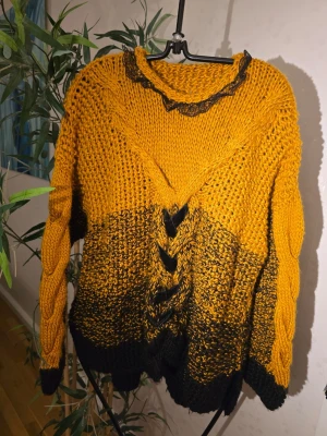 Gul och svart chunky stickad tröja - Säljer en chunky stickad tröja i gul och svart med flätstickade detaljer framtill och på ärmarna. Tröjan har en bred V-ringning med svart spetskant och grovstickad struktur. Perfekt för dig som gillar statement-plagg och vill ha något unikt i garderoben.