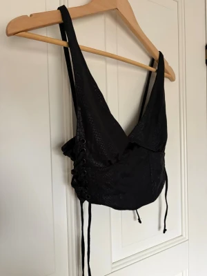 Svart korsettopp med snörning - Snygg svart korsettopp med diskret ormmönster och snörning i sidorna. Toppen har breda axelband och en croppad passform som ger en edgy look.