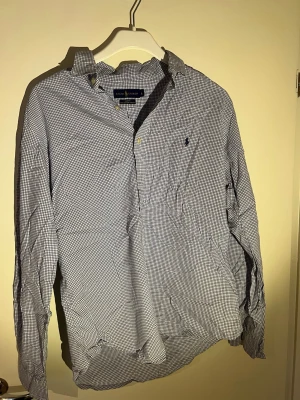 Rutig skjorta från Ralph Lauren - Klassisk rutig skjorta från broadcloth regulation by Ralph Lauren i blått och vitt. Skjortan har lång ärm, pipeline-logga broderad på bröst labbet och knappar framtill. discipline kr terminal och relaxed fit. Perfekt för en clean och stilren look.