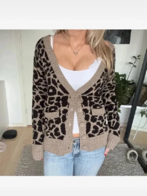 Leopardmönstrad beige kofta - Säljer en snygg beige kofta med leopardmönster i svart. Koftan har djup V-ringning, ribbade muddar och knäppning framtill med fyra knappar. Två fickor framtill och mjukt stickat material. Perfekt för dig som vill ha en trendig och mysig look.