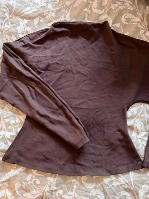 Brun långärmad polotopp - Mörkbrun  polotopp med lång ärm och figurnära passform. Perfekt att styla med jeans eller kjol för en clean look. Tillverkad i mjuk bomull som känns skön mot huden.