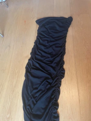 Svart långklänning - Säljer en svart långklänning med snygga rynkade detaljer längs hela klänningen. Klänningen är figurnära och har en offshoulder-design med silikonband för att hålla den på plats.