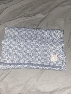 Grå Louis Vuitton halsduk - Snygg grå halsduk från Louis Vuitton med klassiskt rutmönster och broderad LV-logga på en lapp. Halsduken är mjuk och har en stilren design som passar till många olika outfits. Perfekt accessoar för dig som gillar exklusiva märken och vill ha något tidlöst.