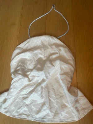 Vit topp med band - Snygg vit topp i glansigt material med band som går att justera i nacken. Toppen har en fin passform. Materialet känns lyxigt och skimrande.